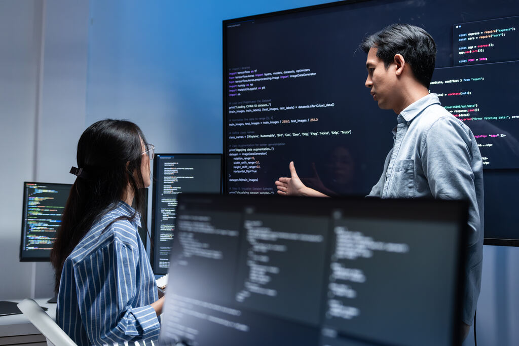 Equipe de desenvolvedores analisando código em monitores, simbolizando escolha de parceiro de tecnologia, suporte especializado e gestão de projetos de TI.